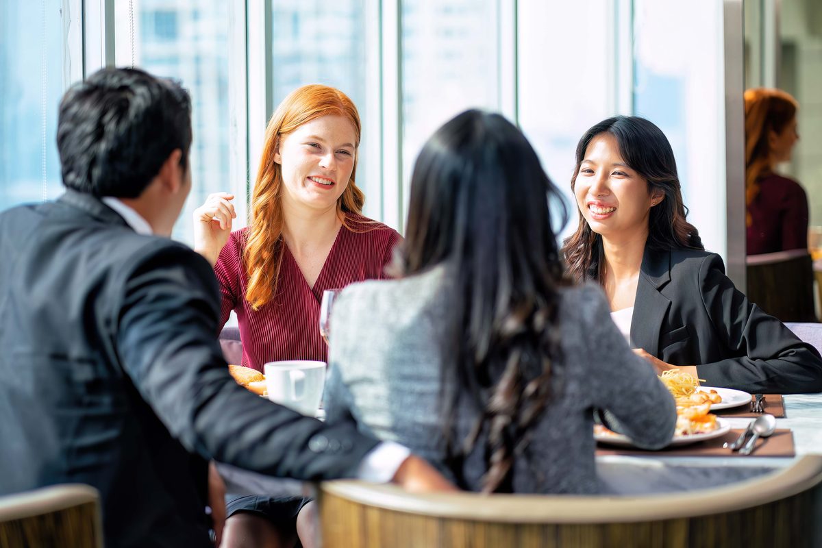 a diverse group of business professionals enjoying a casual meal together in a modern high-rise office setting, with…