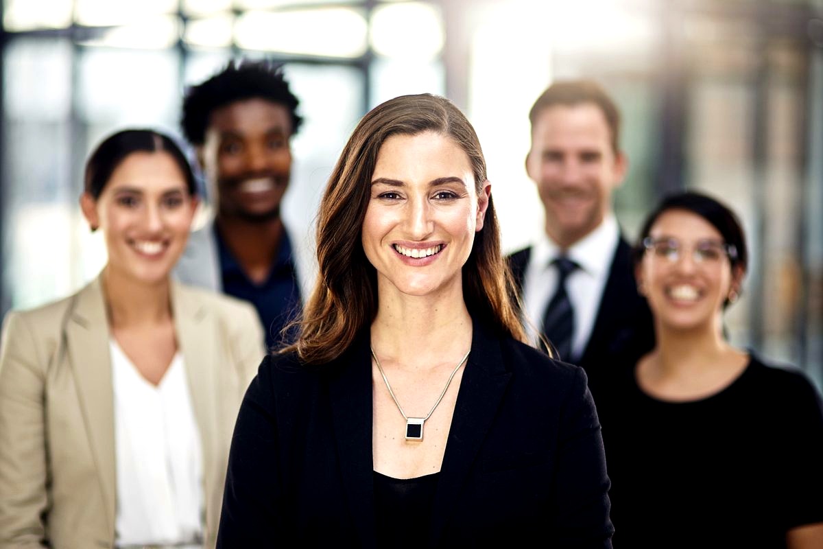 a diverse group of five professional business people in an office setting, with a smiling woman in a black blazer…