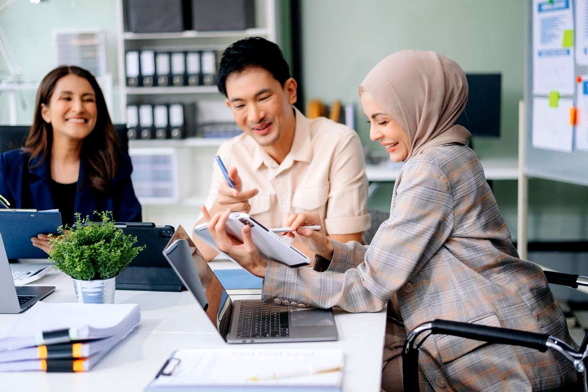 # Image Description
This image shows three diverse young professionals collaborating in a modern office setting, with a…